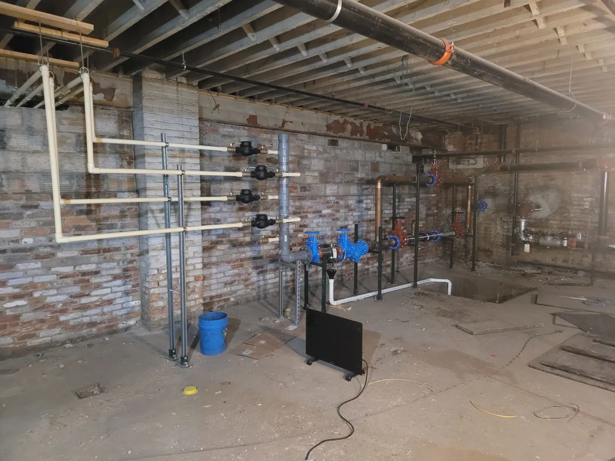 A mechanical room wall carrying a bank of water meters and backflow preventer assemblies, with a grooved-coupling steel main overhead.