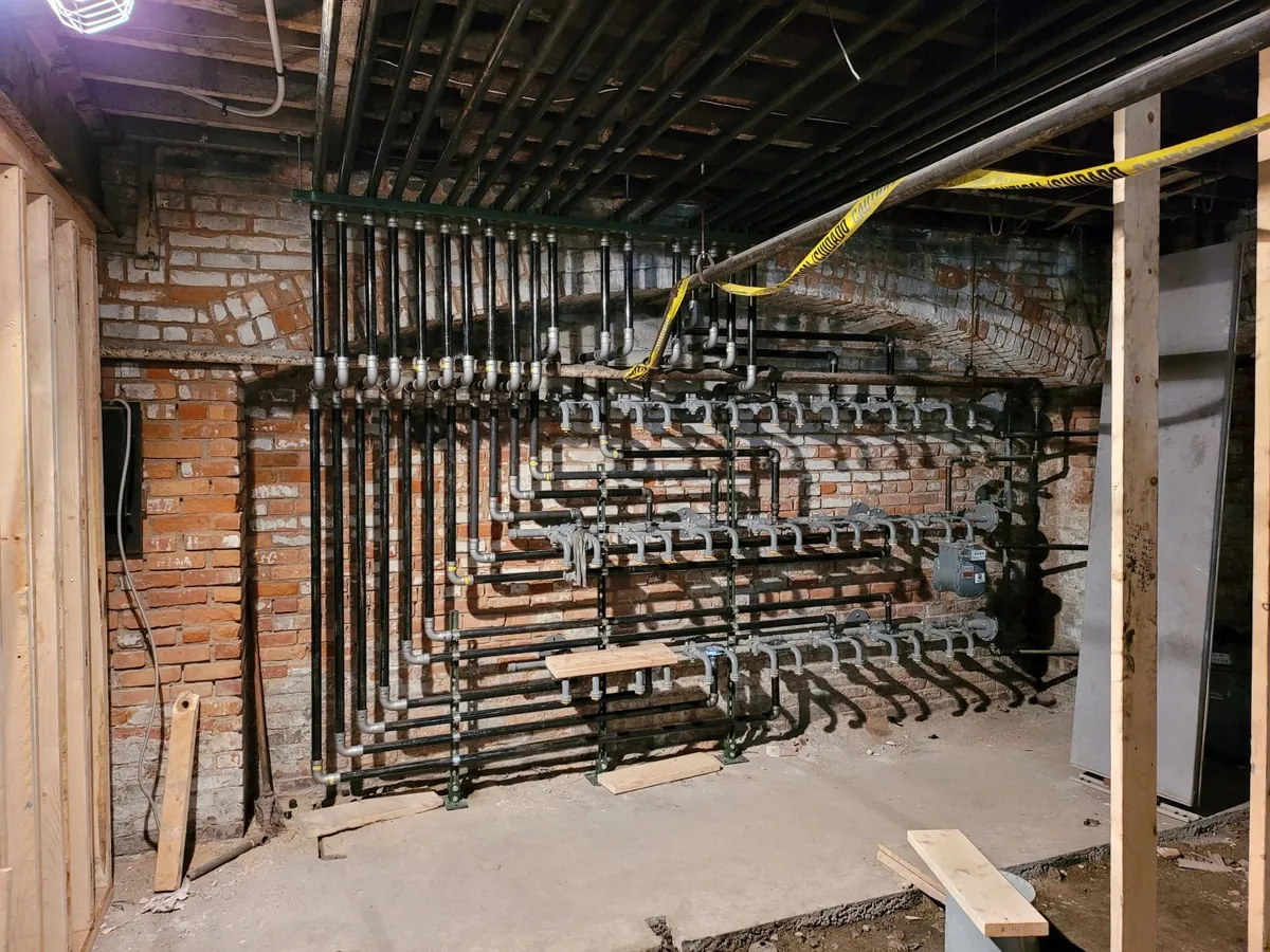 A wall of vertical pipe risers on a manifold, each with its own shutoff valve, mounted against exposed brick in an unfinished basement.